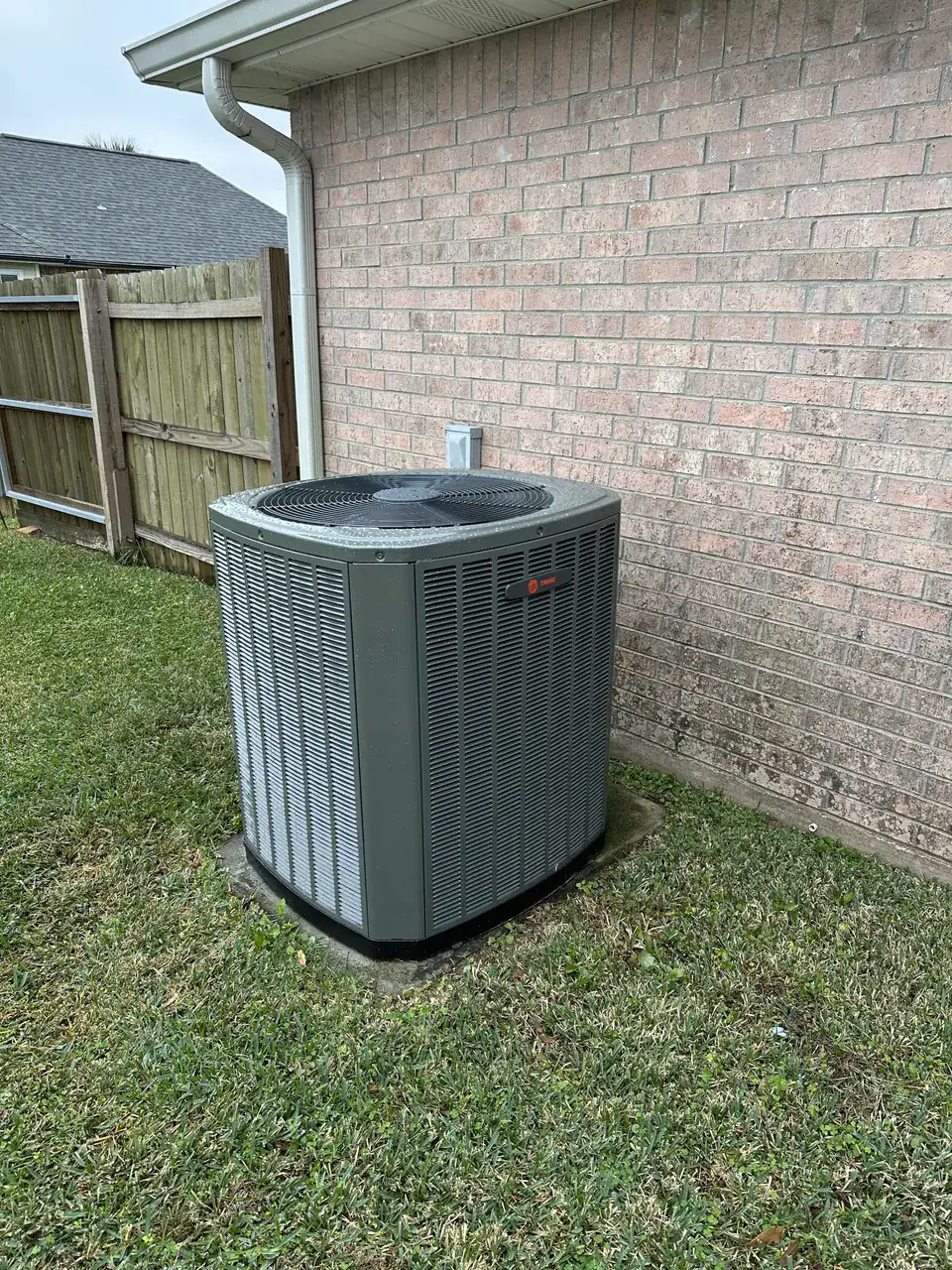 Outdoor HVAC unit beside a light brick home and wooden fence