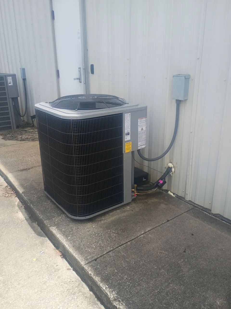 Outdoor HVAC unit on a concrete walkway beside a metal building
