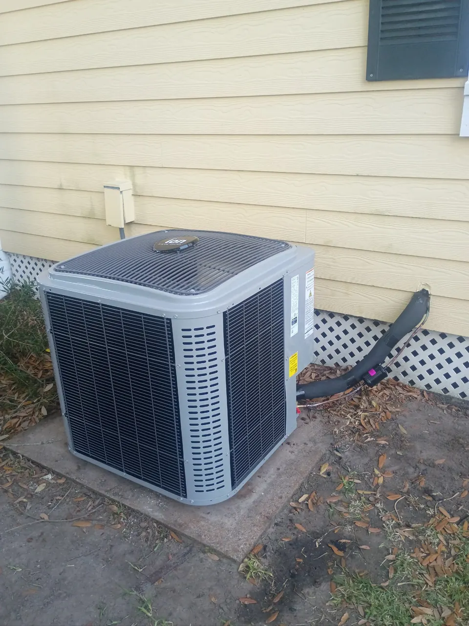 Outdoor HVAC unit beside pale siding with an insulated line connection